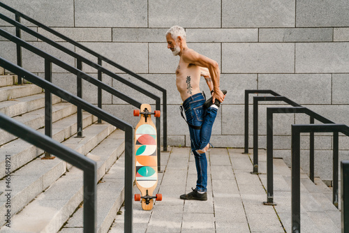 Shirtless man doing warmup while standing with skateboard on stairs photo