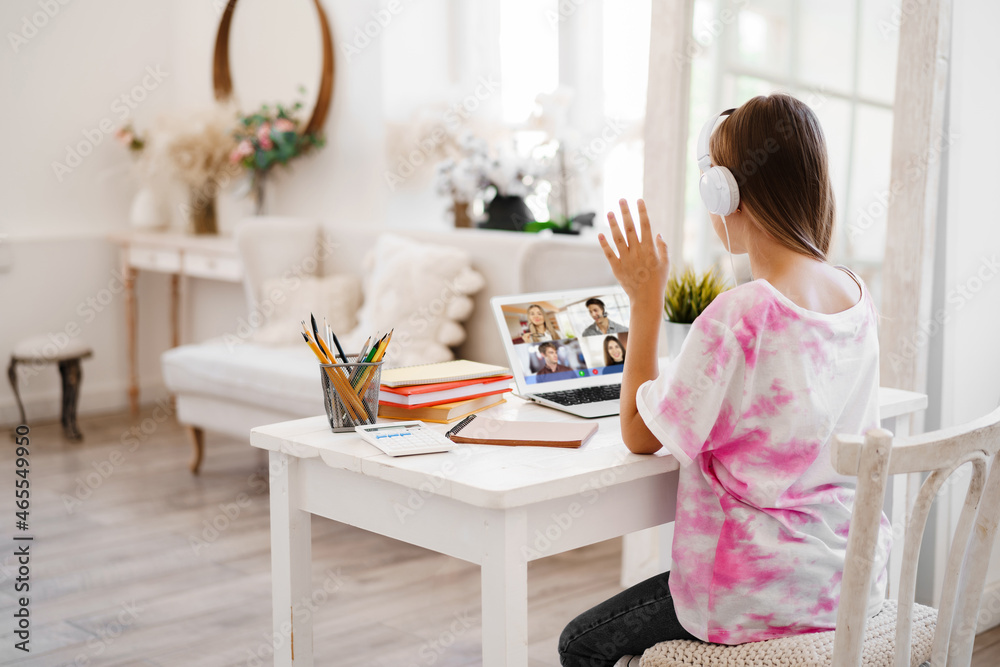 A girl is communicating via video call with classmates on laptop at home