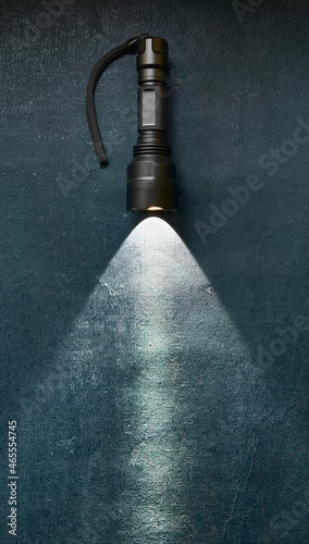 Tactical flashlight shines with bright beam on grunge dark blue background