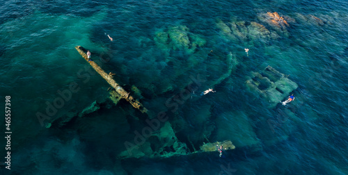 View from above, stunning aerial view of some people swimming and snorkeling around the Chrisso wreck lying on the bottom of the sea. Sardinia, Italy.