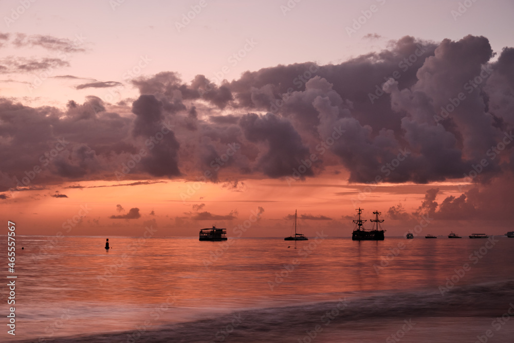 Ships off the coast under a large cloud during dawn.