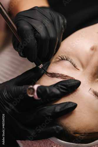 eyebrow microblading. A master in black gloves holds a blending needle over the brow of the model. Macro photography
