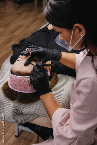 eyebrow microblading. A master in black gloves holds a blending needle over the brow of the model. Macro photography