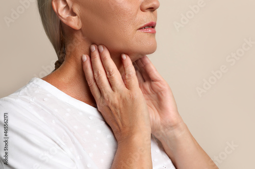 Tableau sur toile Mature woman doing thyroid self examination on beige background closeup