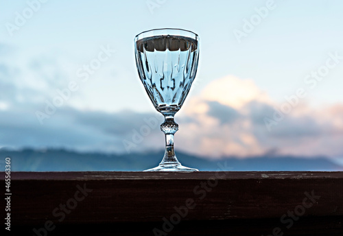 Glass goblet with pure fresh drinking water on light blue background of the sunset sky on wooden table copy space