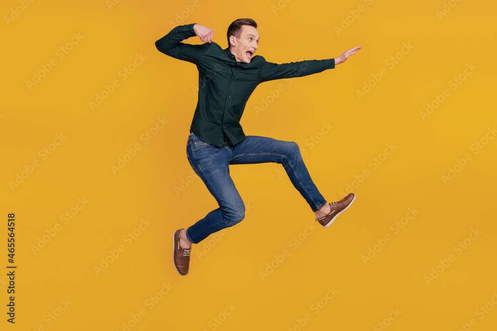Full body profile side photo of young crazy man look empty space kick jump up isolated over yellow color background