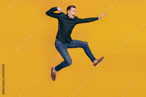 Full body profile side photo of young crazy man look empty space kick jump up isolated over yellow color background © Tetiana