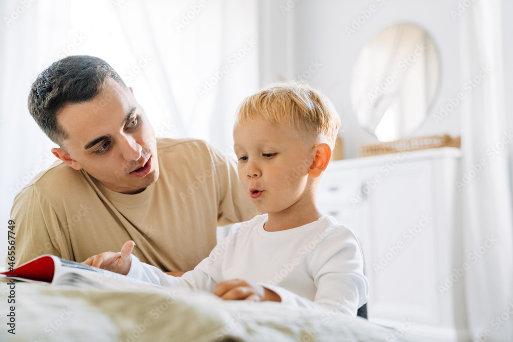 Young white father reading book with his son while sitting on floor