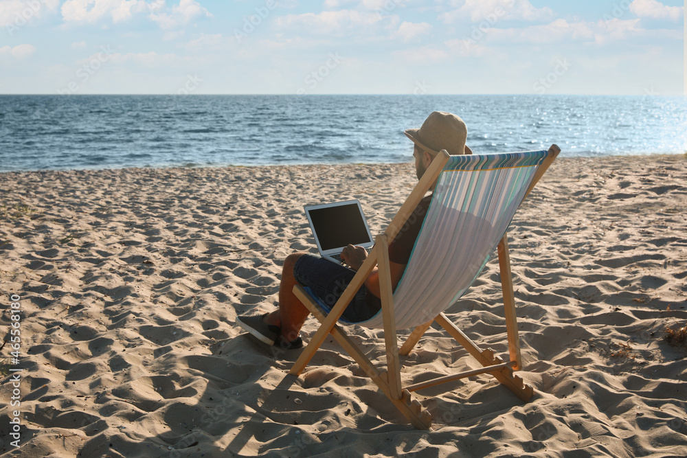Man working with laptop in deck chair on beach. Space for text