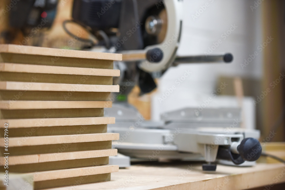 Selective focus on pile of planks with saw in background