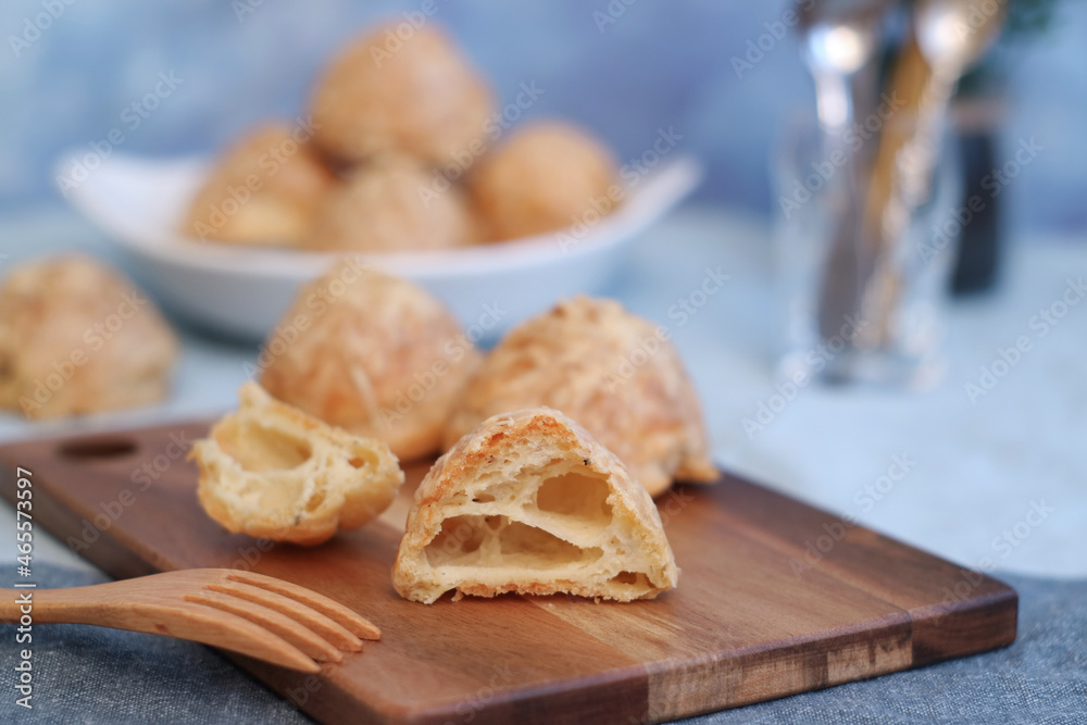 French Gougères in a wooden plate with a cut piece and wooden fork. It's a traditional pastry made with savory choux dough.