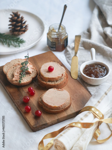 Selective focus of tradtional French foie gras and toaster bread on a wooden plate with Christmas decoration aside with onion marmalade for a festive celebrate.