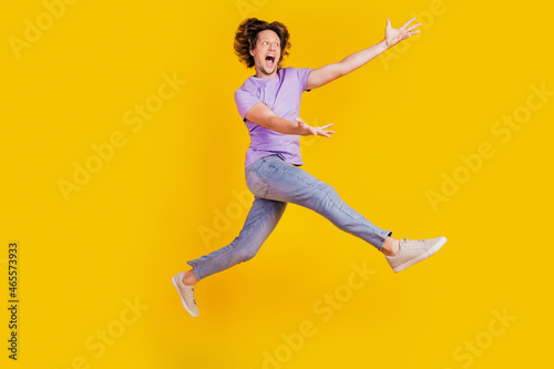 Photo of nice inspired man jump raise hands empty space go wear casual jeans clothes on yellow background
