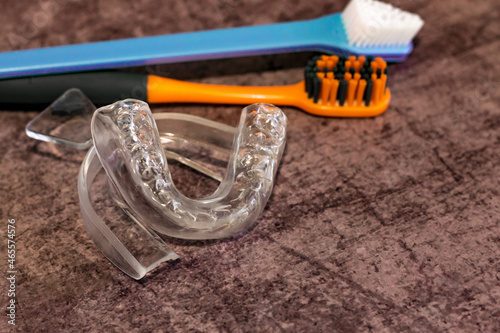on a lilac background there is adental  mouth guard and two toothbrushes next to it; a silicone impression of teeth and an unused mold for the treatment of bruxism and against night snoring
