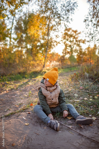 Inquisitive boy with a stick sits on the path and has rest during explores beautiful forest exploring. Outdoor lifestyle, active family lifestyle. Autumn road trip, outdoor lifestyle © Maria
