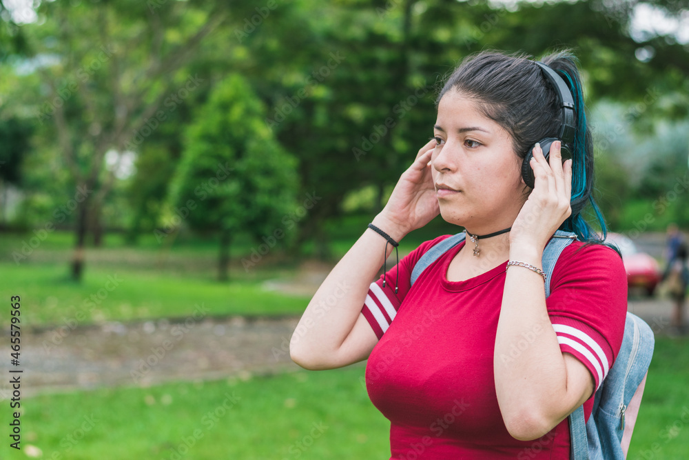 beautiful college woman with blue hair and red dress, listening to music with her wireless headphones in a park, pensive with her hands gripping the headphones. concept of freedom beautiful college woman with blue hair and red dress, listening to music with her wireless headphones in a park, pensive with her hands gripping the headphones. concept of freedom