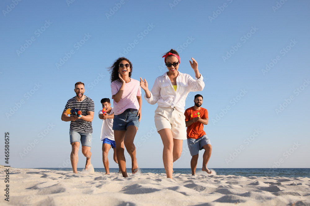 Group of friends with water guns having fun on beach