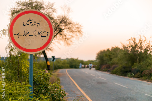 Sign board in Urdu language to slow down the traffic before sharp turn 