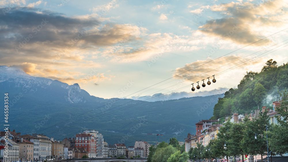 The silhouette of the famous cablecar in Grenoble, France, crossing the picture in diagonal. European alps in the background, with blue sky and white clouds at sunset. With copy-space.