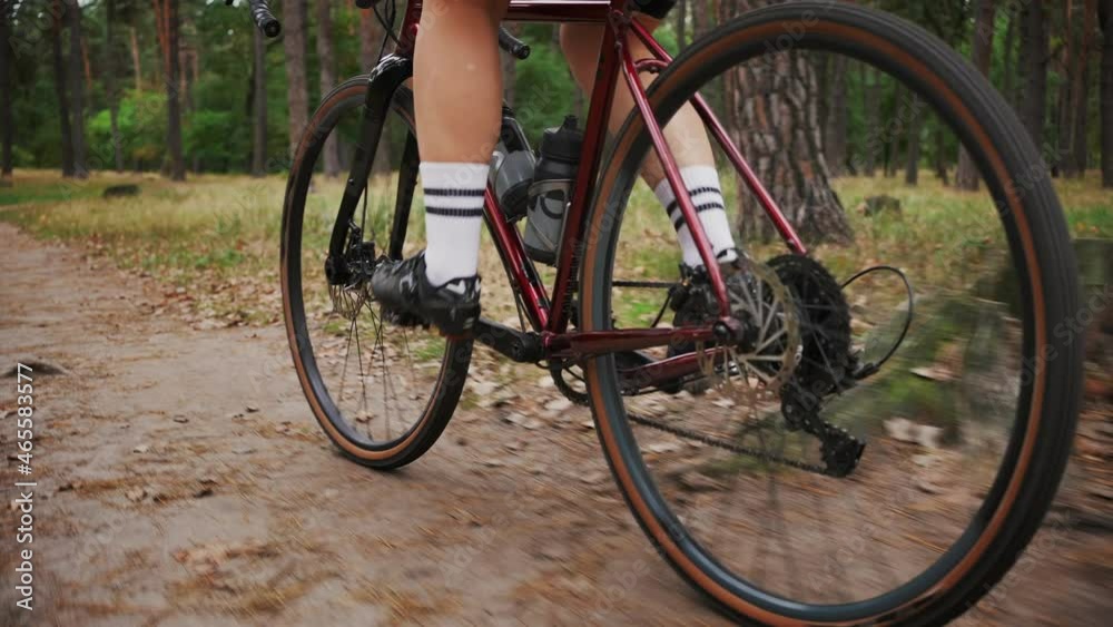 Unrecognizable woman athlete riding bicycle in autumn forest, pedaling red sports bike on rural path, tracking shot Unrecognizable woman athlete riding bicycle in autumn forest, pedaling red sports bike on rural path, tracking shot