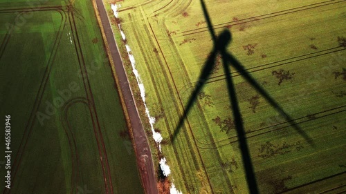 Aerial view of a field with the rotating shadow of a wind turbine