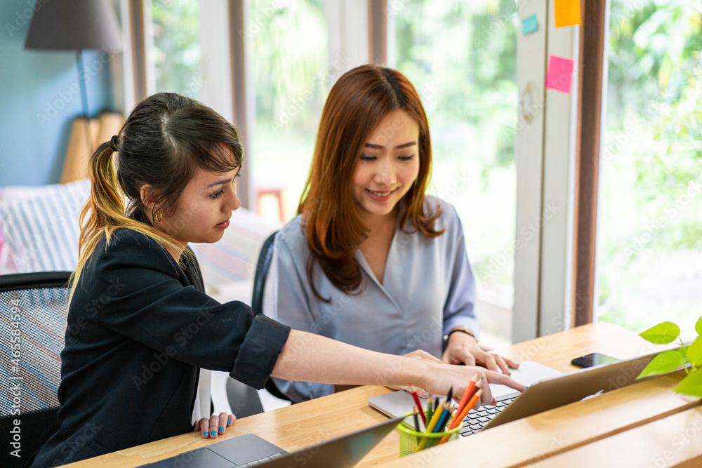 Obraz premium Asian businesswoman using laptop computer co-working with her team in a busy business corporate modern office. workspace and shared office, diverse women coworkers and office together concept