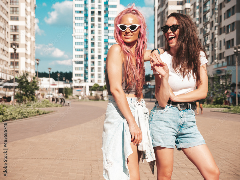 Two young beautiful smiling hipster female in trendy summer clothes.Sexy carefree women posing in the street with pink hair. Positive pure models having fun at sunset. Cheerful and happy