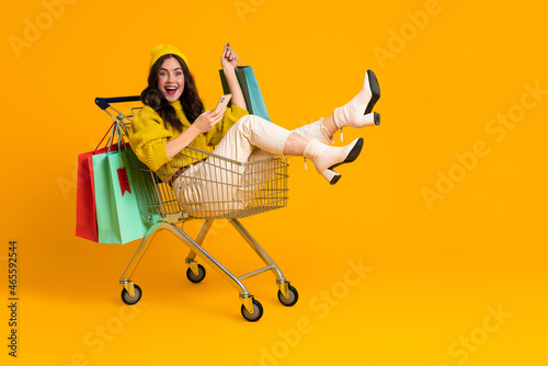 White excited woman laughing and using cellphone in shopping cart