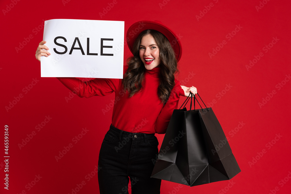 White woman smiling while posing with shopping bags and sale placard White woman smiling while posing with shopping bags and sale placard
