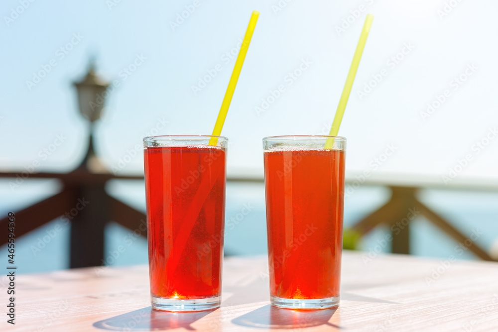 Two glasses with berry juice and strawberries on the table of a street cafe against the background of the sea. Two glasses with berry juice and strawberries on the table of a street cafe against the background of the sea.