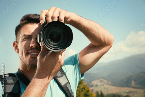 Professional photographer taking picture with modern camera in mountains, focus on lens © New Africa