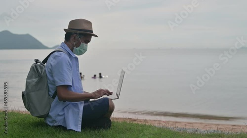 Man wear mask using laptop computer on beach  sea  and Man travel holiday Phuket sandbox Thailand are freedom life financial