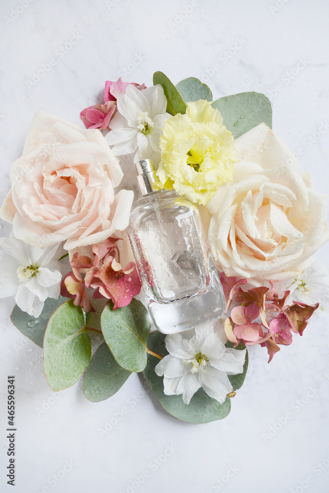 Square bottle of perfume with white roses, pink hydrangea, eucalyptus branch, water drops on the white background.  Summer, spring flower smell. Perfume inside different flowers wreath. Girlish smell.