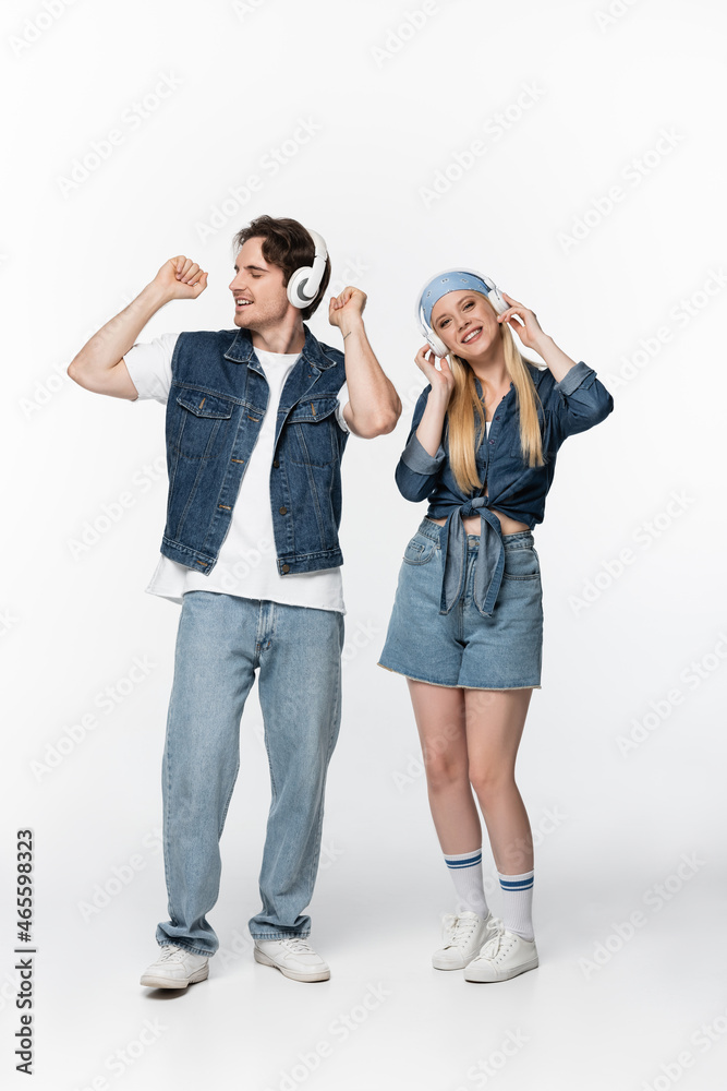 full length view of trendy and joyful couple in wireless headphones listening music on white full length view of trendy and joyful couple in wireless headphones listening music on white