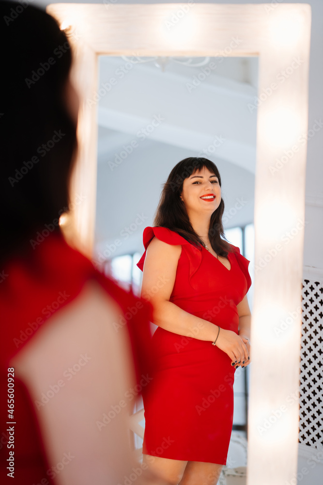 an attractive chubby woman in a red dress looks in the mirror. an attractive chubby woman in a red dress looks in the mirror.