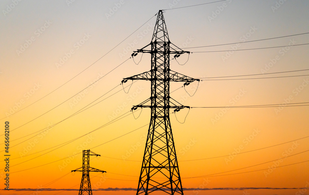 Fototapeta premium High voltage towers and power lines against orange sunrise sky.