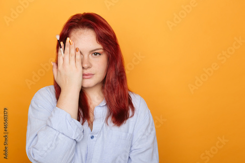 Closeup portrait of young visagist with makeup brush in hand. Red-haired girl isolated on orange. Professional