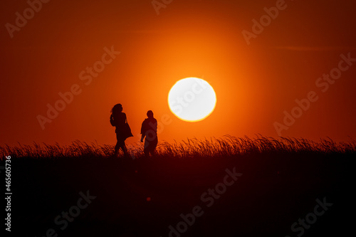 Silhouettes of people walking on grass on sunset with back lite and sun on backgound