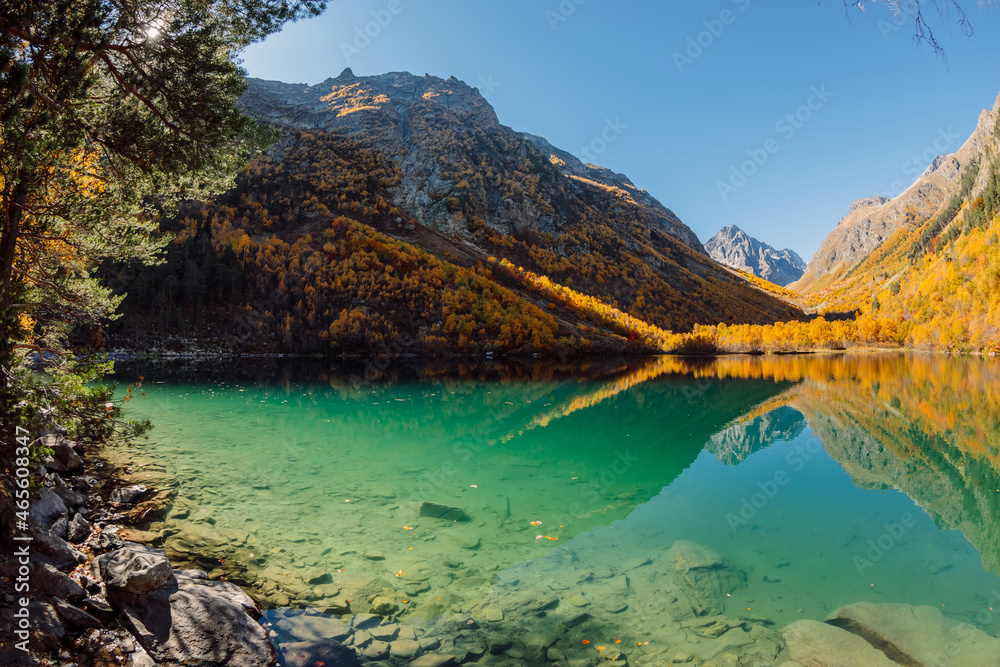 Mountain lake with transparent water and autumnal trees on mountains