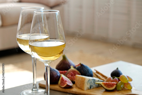 Two wineglasses of vintage chardonnay with delicious appetizers. Couple of glasses of white wine, italian breadsticks, figs and grapes. Interior background. Close up, copy space. photo