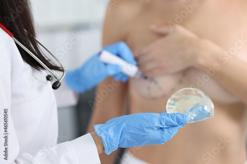 Plastic surgeon holding silicone breast implant and applying preoperative markings to patient chest closeup