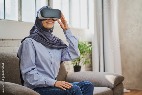 Joyful Arabian woman sitting on a couch, wearing a VR helmet and smiling