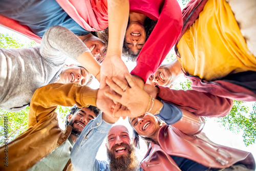 directly below portrait of happy diverse large group of multicultural friends holding hands making high five stacking them together outdoors. convivial people having fun. friendship, lifestyle concept