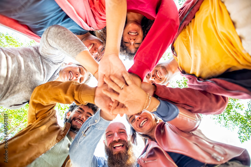 directly below portrait of happy diverse large group of multicultural friends holding hands making high five stacking them together outdoors. convivial people having fun. friendship, lifestyle concept photo