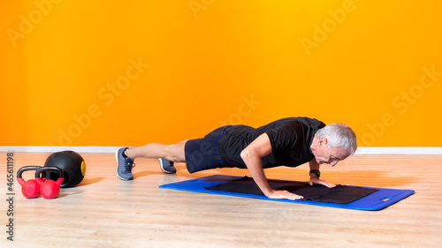 focused senior fit man doing push up workout exercise laying at the gym isolated on orange background. mature people fitness training indoor. elderly person recovery healthy lifestyle concept