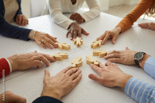 Group of multiethnic business people and teammates sitting around office table put little wooden human figures in circle as symbol of community, team, help, cooperation, collaboration and teamwork photo
