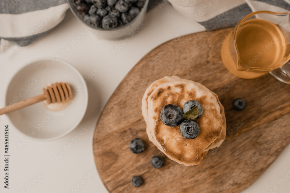 Pancakes with maple syrup and blueberries on wood on a light background, copy space. Summer homemade breakfast. Pancakes with maple syrup and blueberries on wood on a light background, copy space. Summer homemade breakfast.