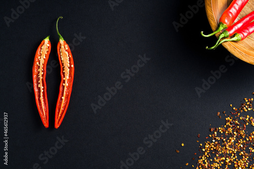 Single Red Hot Chilli Pepper cut lengthways with seeds placed on low key black minimalistic background with bunch of chillies in the wooden bowl photo