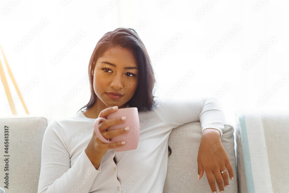 Beautiful smiling American woman at home sitting on sofa drinking cup of coffee