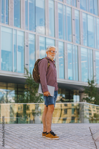 an adult gray-haired man with a beard goes to the office to work. a senior businessman in a shirt and with a laptop is making a career in a large company. a stylish European talks on the phone with